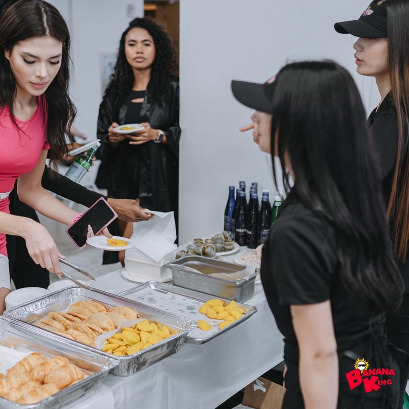 People serving themselves fast-food items like empanadas and plantains from a buffet table.