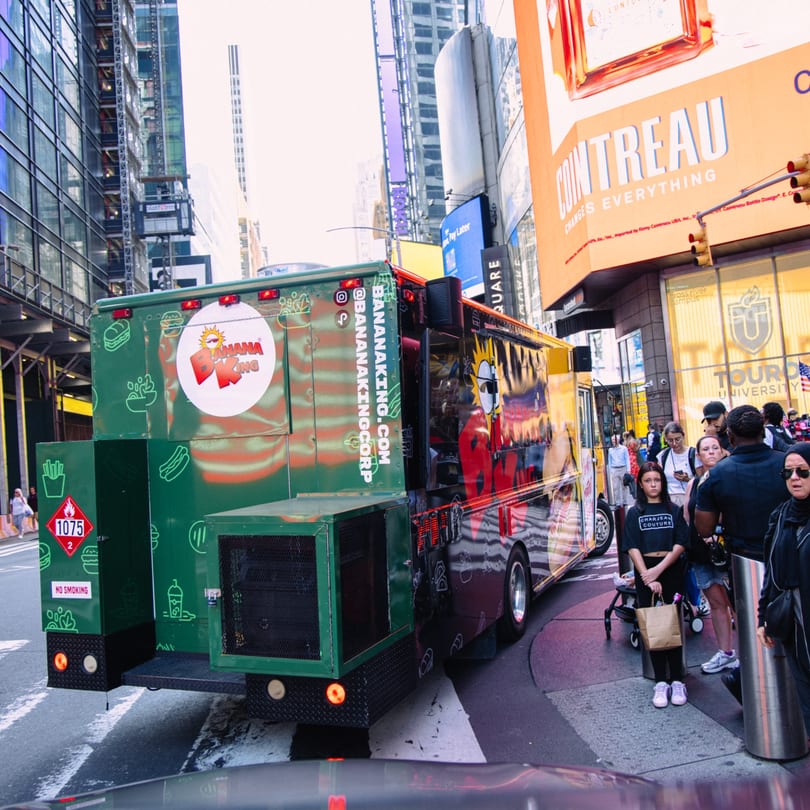 Banana King food truck parked on a busy city street with people and tall buildings.