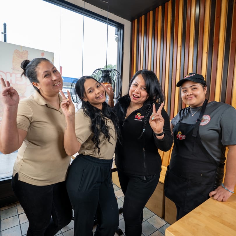 Four smiling Banana King restaurant employees pose together, making peace signs at the camera.