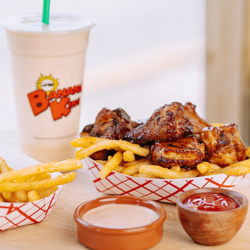 Banana King's BBQ ribs and fries in paper trays, with dipping sauces and a banana milkshake.