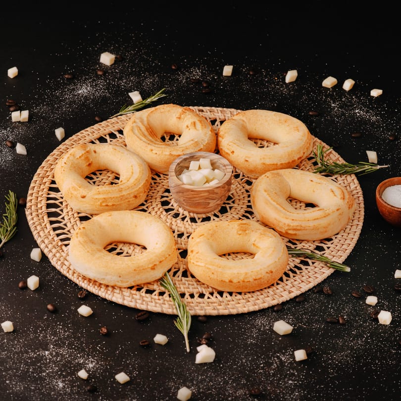 Six golden-brown ring-shaped breads on a woven mat with sugar cubes and rosemary sprigs.