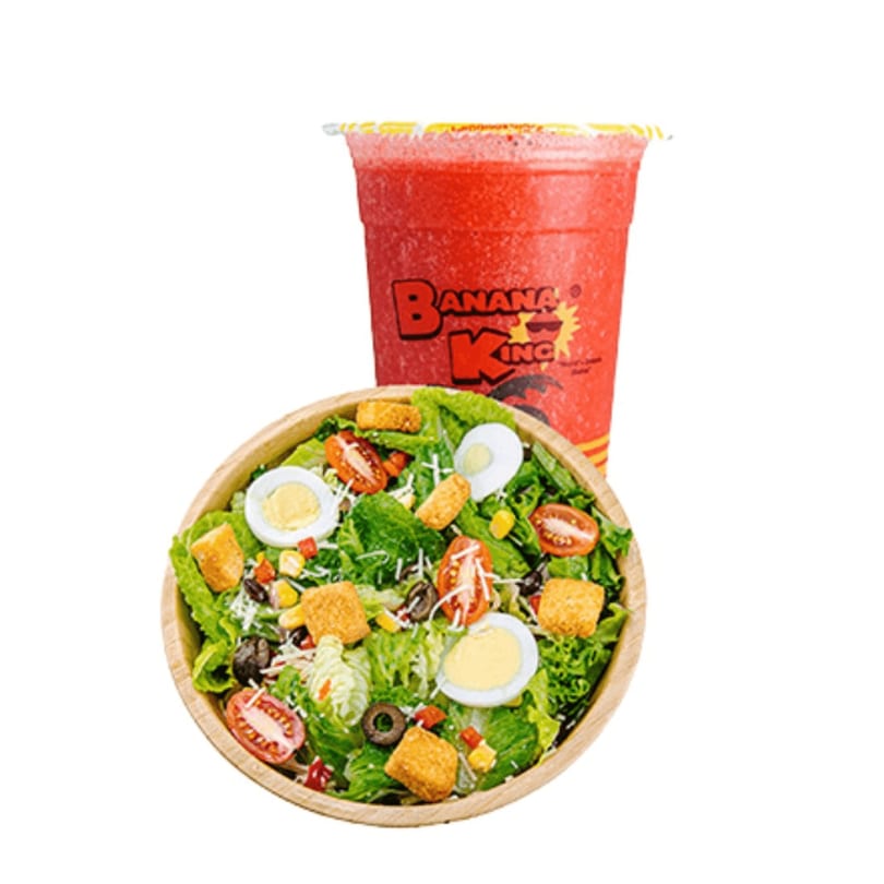 A Banana King branded red slushy drink next to a fresh salad with eggs, tomatoes, and croutons.