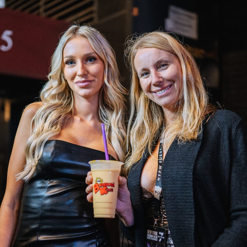 Two women smiling, one holding a Banana King smoothie with a purple straw.