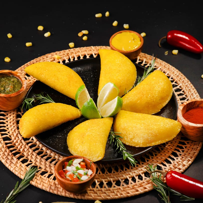 Golden empanadas arranged on a black plate with lime wedges, surrounded by various sauces and spices.