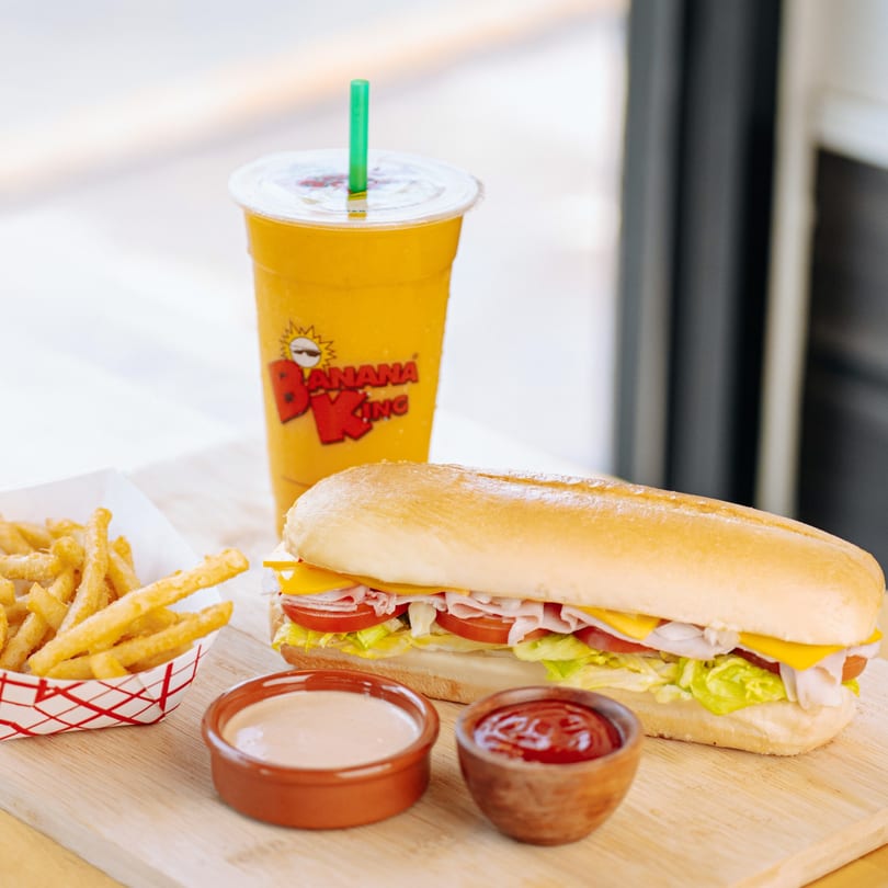 Banana King fast-food meal with a sub sandwich, fries, dipping sauces, and a branded mango smoothie.