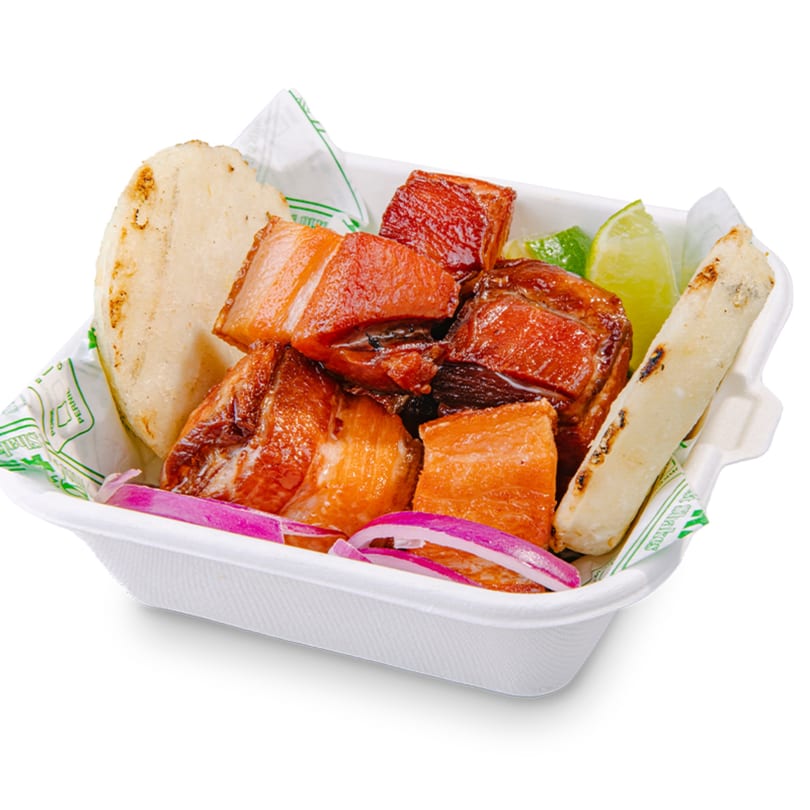 Banana King's fried pork belly chunks with tortillas, lime wedges, and red onion in a take-out container.